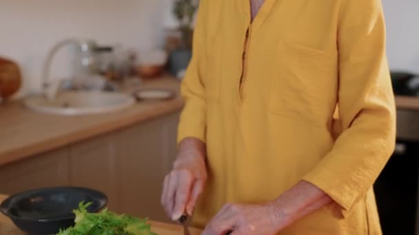 コットンマスタードのコーカサスシニアの女性の中型ショットをキルティングし 自宅で健康的なランチや夕食を作っている間に新鮮な野菜を切るドレス — ストック動画