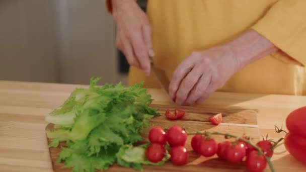 日中キッチンで調理テーブルで木の切断板に新鮮なチェリートマトを切断する認識できない老婆のクロップショット — ストック動画
