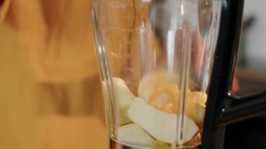 Tanımlanamayan yaşlı bir kadının taze elma ve portakalı blender 'a koyup sabah detoks smoothie yaparken görüntüsü.