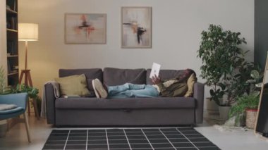 Gündüz vakti modern dairede rahat bir şekilde kanepede uzanan yetişkin bir zenci ve dijital tablet bilgisayardan video çağrısının tam görüntüsü.