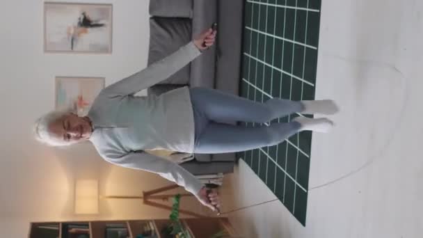 現代のリビングルームで国内のカーディオワークアウトをしながらロープをスキップするアクティブな白人シニア女性の垂直フルショット — ストック動画