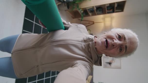 国内のフィットネストレーニング中に腕の記録ビデオブログの下にロールヨガマットを持つ古い白人女性の垂直ハンドヘルドPovショット — ストック動画