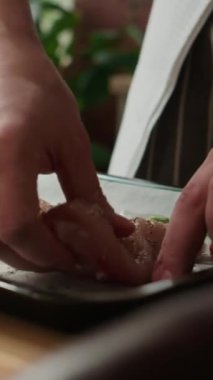 Mutfaktaki ahşap yemek masasında ızgara biberiyeli tavuk hazırlayan tanınmayan şefin dikey kırpılmış görüntüsü.