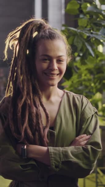 若い白人女性の垂直中型のスローモの肖像画 バックグラウンドの多くの植物を植物工場で折った手でポーズするドレッドロック — ストック動画