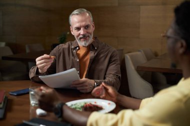 Olgun iş adamı, iş yemeği sırasında iş arkadaşıyla kafede yaptığı toplantıda iş sözleşmesinin şartlarını tartışıyor.
