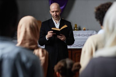 Vaftizci kilisesinde mihrabın yanında duran inançlılar için İncil okuyan siyah takım elbiseli olgun bir vaiz.