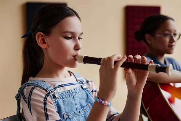バックグラウンドで他の学生と音楽クラスでフルートを演奏することに集中する少女 — ストック写真