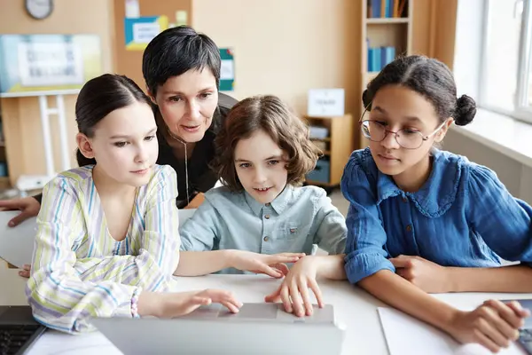 Mature teacher discussing online presentation on computer together with children during lesson in class