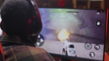 Uzman kulaklıklı Afro-Amerikan erkek oyuncunun gece vakti evdeki masaüstü bilgisayarında FPS oyunu oynarken arka plan görüntüsü ortamı kapatması