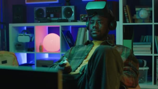 美国黑人男子头戴Vr耳机 晚上在霓虹灯室内玩虚拟游戏时开始操作控制器的中景照片 — 图库视频影像