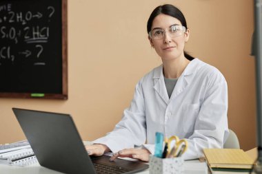 Sınıfta dizüstü bilgisayar kullanırken kameraya bakan kadın fen öğretmeni portresi, boşluğu kopyala