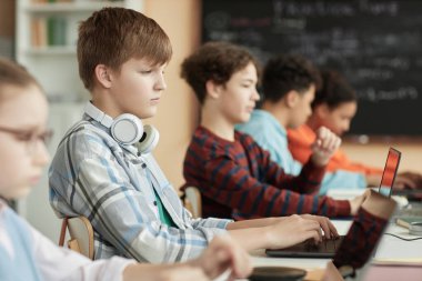 Sınıfta sırayla bilgisayar kullanan ve çevrimiçi sınava giren bir grup çocuğun yan görüntüsü