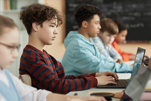 Вид сбоку на подростка, использующего компьютер в классе и сдающего онлайн-экзамен
