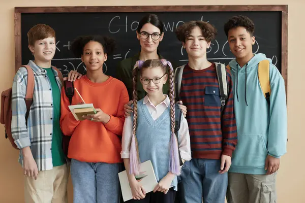 stock image Front view portrait of diverse group of children looking at camera standing by blackboard in class