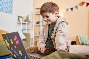 Evde internet kullanırken bilgisayar ekranına bakan gülümseyen çocuğun yan görünüm portresi