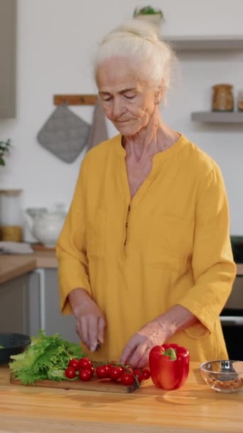 キッチンで調理テーブルに立って新鮮な野菜を切って 自宅でランチにサラダを作っている健康な白人高齢女性の垂直ショット — ストック動画