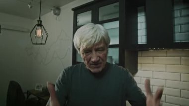 Öfkeli Kafkasyalı yetişkin bir adam mutfakta durup kollarını sallarken karısına bağırıyor.
