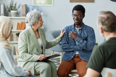 Young African American man describing his psychological problem to counselor and other patients of course while sitting in front of them clipart