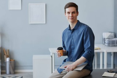 Ofiste kahve fincanı ile otururken kameraya bakan genç işadamının portresi.