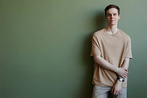 Minimal portrait of young man dressed in comfortable outfit looking at camera against green, copy space