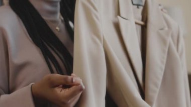 Tasarımcı dükkanında alışveriş yaparken bej renkli şık ceketi müşteriye gösteren tanınmayan kadın moda tasarımcısının yavaş çekimleri.