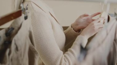 Kendine güvenen genç, beyaz tenli moda tasarımcısının arka plan yavaş çekimi elbise rafının yanında duruyor, kanalı için yeni video çekerken moda öğelerini kamerada gösteriyor.