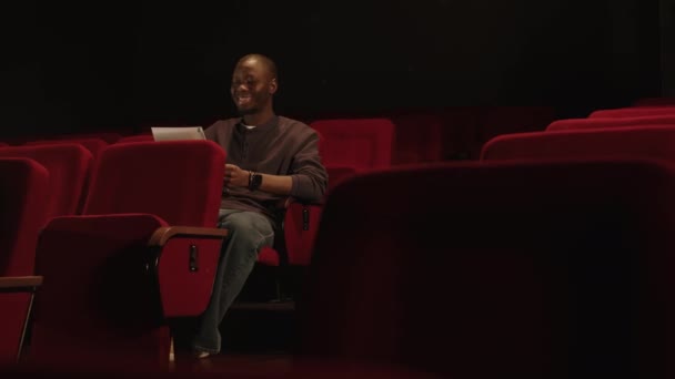 劇場で赤い座席に座っている間 彼のモノローグをリハーサルする若い才能のある黒人のスペースショットをコピー — ストック動画