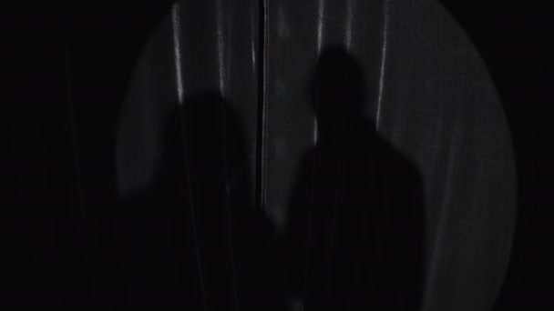 两个难以辨认的黑人阴影笼罩在黑暗的窗帘上 在舞台上聚光灯下表演喜剧 — 图库视频影像