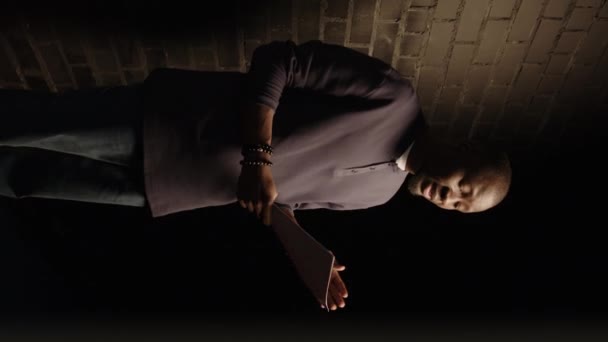 暗い廊下のレンガの壁に立ち 劇場でのオーディション前に再生スクリプトをリハーサルする若いカリスマ的な黒人俳優の垂直ショット — ストック動画