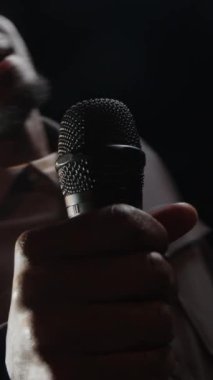 Mikrofonla konuşan genç siyahi erkek stand-up komedyeninin karanlık sahnede sahne ışıklarıyla görüntüsü.