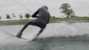 Dalgıç kıyafetli ve miğferli profesyonel wakeboardcunun gölde su sıçratırken elinde ip tutarken tam görüntüsünü alıyorum.