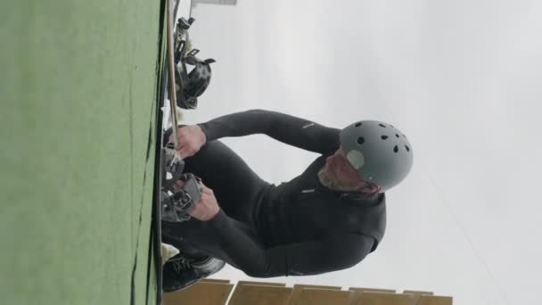 白种人成年男子男子滑板冲浪运动员在缆绳公园训练时身穿湿衣 头戴钢盔 双膝跪下 在船上搭绳的垂直拍摄 — 图库视频影像