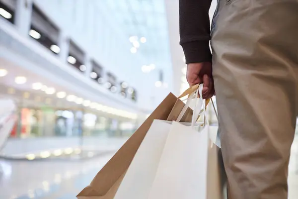 Close up of man holding shopping bags standing in mall interior copy space