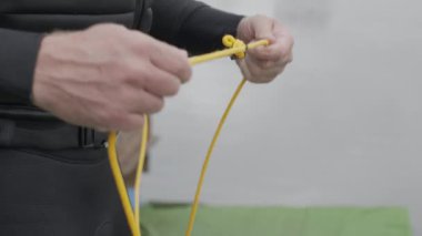 Mayo giymiş tanınmayan bir erkek sörfçünün rıhtımda çözünen wakeboard halatının kırpılmış görüntüsü.