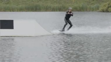 Dalgıç kıyafeti ve miğfer takıp, kablo parkında sürgülü kayma numarası yaparken tam bir wakeboardcu pozu.