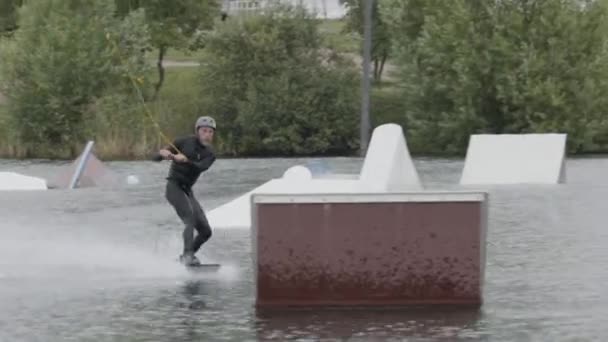スライダーでウェットスーツとヘルメットの練習トリックを着て ケーブルパークでウェイクボードしながら水に落ちるコーカサス成人男性のフルショット — ストック動画