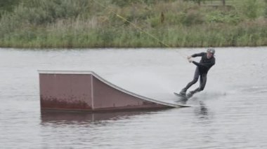 Yetişkin beyaz erkek wakeboardcu, kablo parkında antrenman yaparken sürgüden kayıyor.