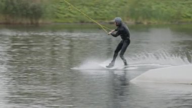 Wakeboard sörfçüsünün kablo parkında wakeboard çalışırken kaydırak numarasını çekerken ki görüntüsü.