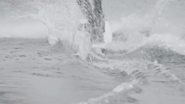 スプラッシュで水を横切ってウェットスーツに保持している認識できない男性サーファーのクロップバックビューショット — ストック動画