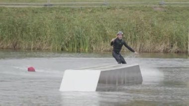 Yetişkin beyaz erkek wakeboardcunun kablo parkında geriye doğru kaydığını gösteren ön görüntü.