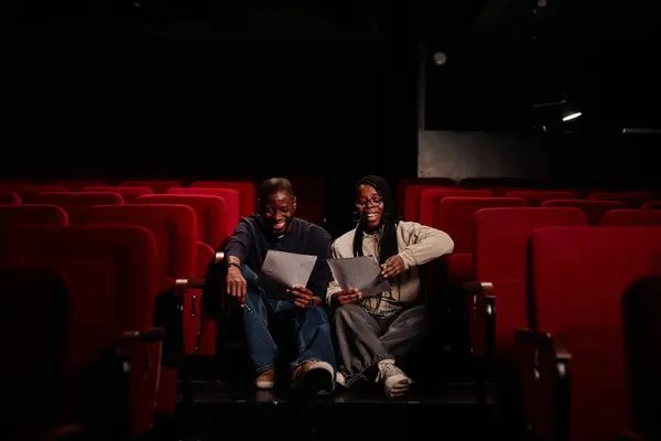 Front view portrait of performers duo rehearsing lines together sitting on floor in theater and smiling copy space