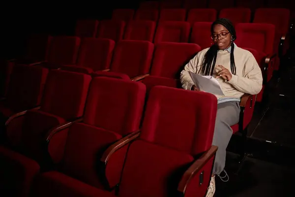 低光コピースペースの劇場で観客の脚本を読んでいる黒人成人女性の最小の肖像画 — ストック写真