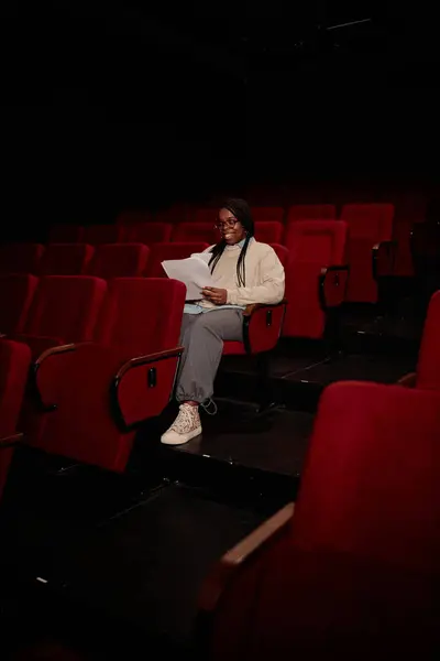 Vertical full length portrait of young woman alone in audience preparing for show and reading script