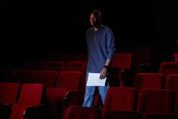 Portrait of Black man walking towards stage in empty theater audience copy space