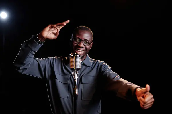 Minimal waist up portrait of emotional African American man speaking to microphone and performing on stage with spotlight copy space