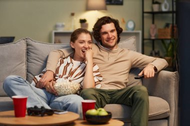 Evde film izleyen ve kanepede oturup patlamış mısır yiyen mutlu genç bir çiftin portresi.