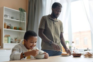 Afro-Amerikan aile portresi baba ve oğulla birlikte mutfak masasında kahvaltı yapıyorlar.
