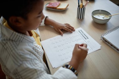 Mutfak masasında ödev yapan ve matematik sınavını çözen Afrikalı Amerikalı çocuğun omzunun üstünden.