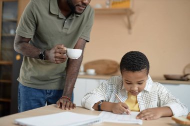 Babasıyla mutfak masasında ödev yapan Afro-Amerikan bir gencin minimum portresi.