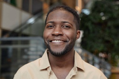 Ofis binasında poz verirken gülümseyen Afrikalı Amerikalı bir adamın ön manzara portresi.